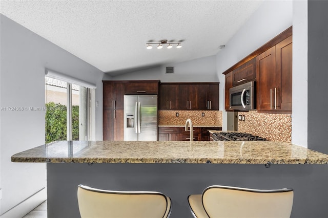 kitchen featuring kitchen peninsula, a textured ceiling, vaulted ceiling, tasteful backsplash, and appliances with stainless steel finishes