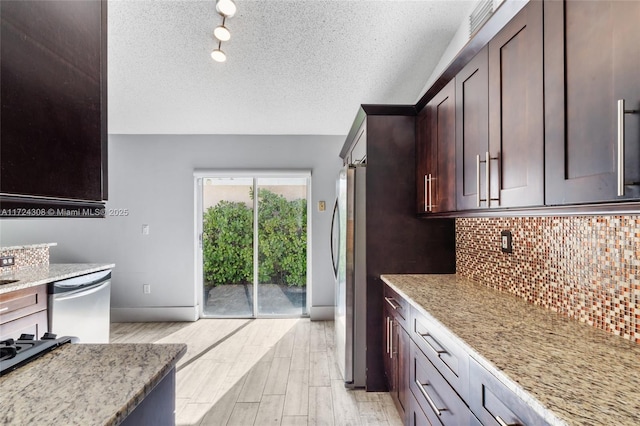 kitchen with light stone countertops, a textured ceiling, light hardwood / wood-style floors, backsplash, and appliances with stainless steel finishes