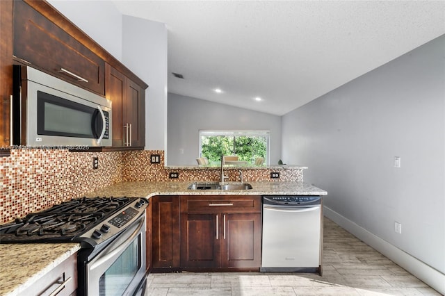 kitchen with stainless steel appliances, sink, vaulted ceiling, light stone counters, and kitchen peninsula