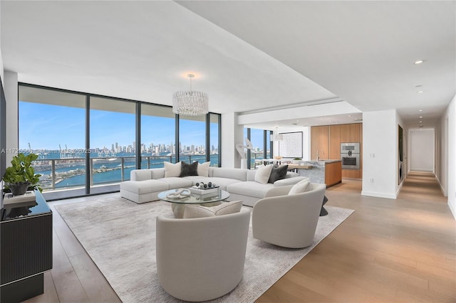 living room with floor to ceiling windows, an inviting chandelier, light hardwood / wood-style flooring, and a water view