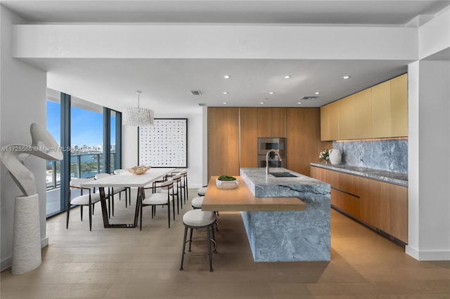 kitchen with sink, decorative light fixtures, light hardwood / wood-style floors, backsplash, and a center island with sink