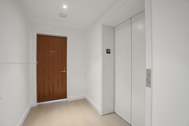 hallway with elevator and light hardwood / wood-style flooring