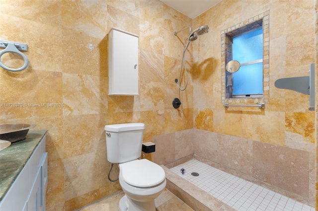 bathroom featuring toilet, a tile shower, vanity, and tile walls