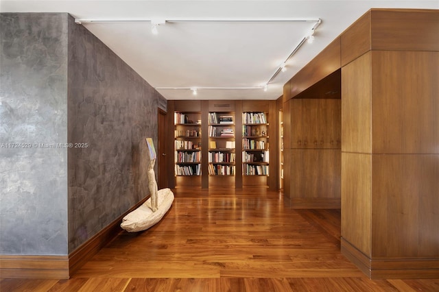 hallway with track lighting, hardwood / wood-style floors, and built in shelves