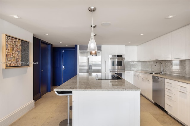 kitchen featuring light stone counters, hanging light fixtures, stainless steel appliances, a kitchen island, and sink