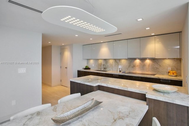 kitchen featuring sink, light stone counters, a breakfast bar area, decorative backsplash, and black electric stovetop