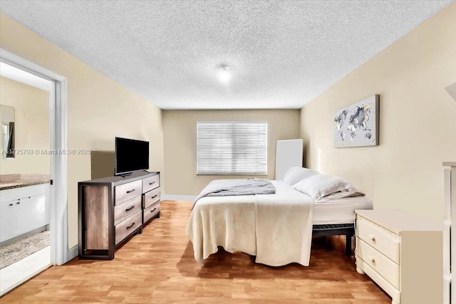 bedroom featuring a textured ceiling, light hardwood / wood-style floors, and connected bathroom