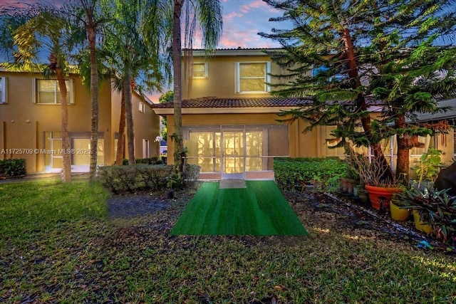 back house at dusk featuring a lawn