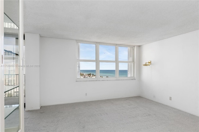 empty room featuring a textured ceiling, light carpet, and a water view