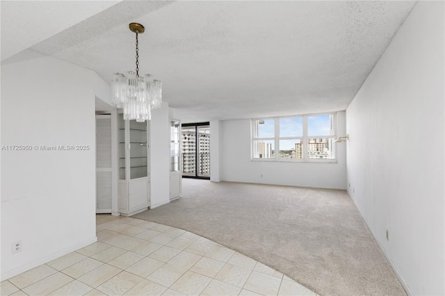 empty room with a textured ceiling, light carpet, and a notable chandelier