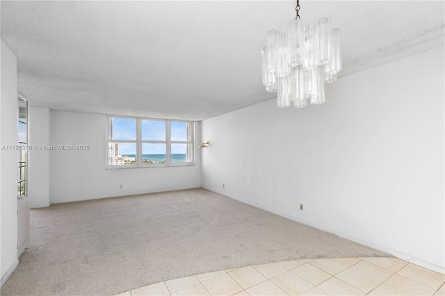 unfurnished room featuring light colored carpet, a textured ceiling, and an inviting chandelier