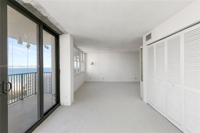 interior space featuring a textured ceiling, light colored carpet, and a water view