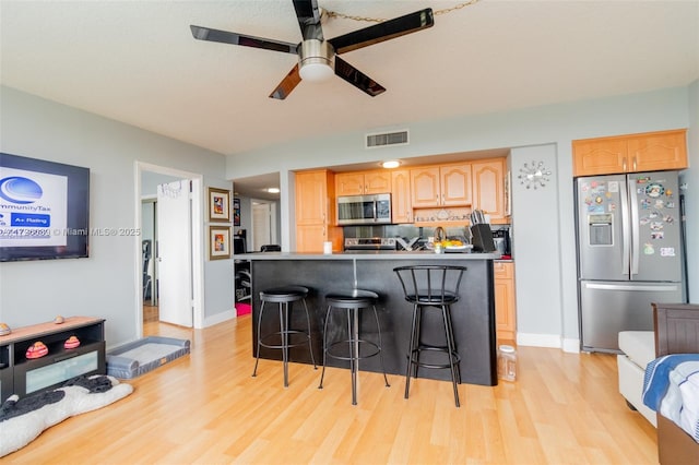 kitchen featuring stainless steel appliances, ceiling fan, a breakfast bar, decorative backsplash, and light hardwood / wood-style flooring