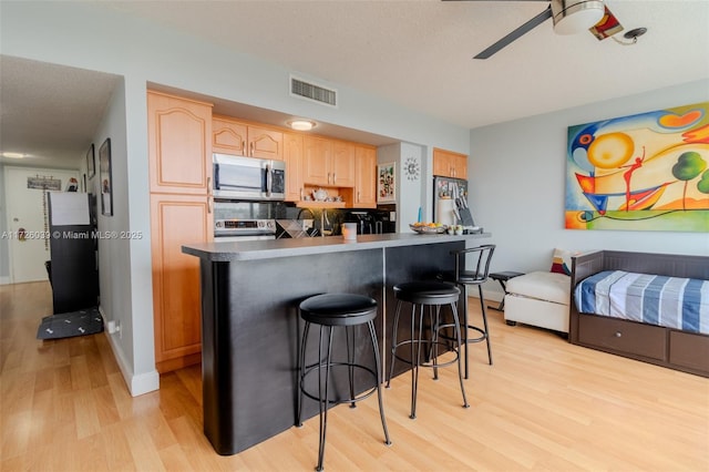 kitchen featuring light hardwood / wood-style flooring, stainless steel appliances, a breakfast bar, decorative backsplash, and ceiling fan