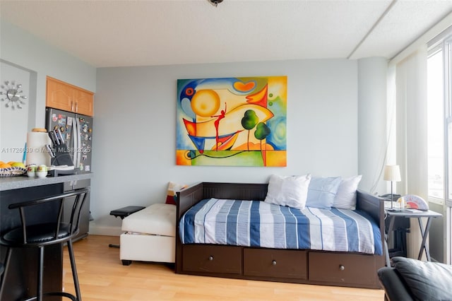 bedroom featuring light wood-type flooring and stainless steel refrigerator