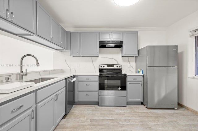 kitchen with gray cabinets, stainless steel appliances, light wood-type flooring, sink, and extractor fan