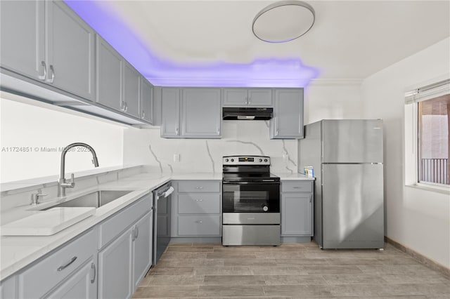 kitchen featuring light stone counters, stainless steel appliances, gray cabinetry, and sink