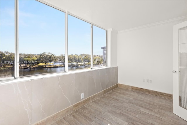 empty room featuring ornamental molding, light hardwood / wood-style flooring, and a water view