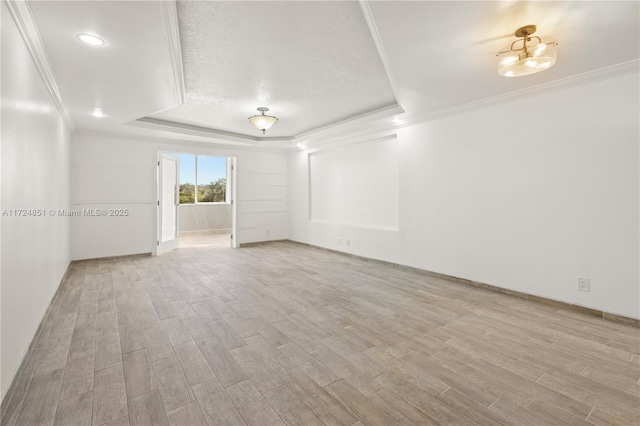 empty room featuring light hardwood / wood-style floors, crown molding, a raised ceiling, and a textured ceiling