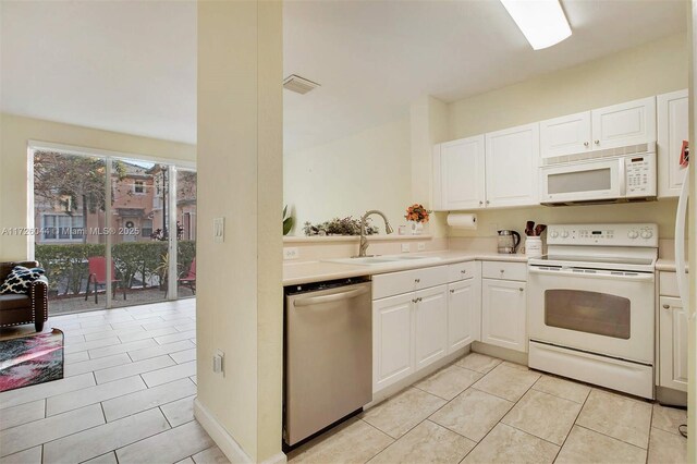 kitchen with sink, white appliances, light tile patterned floors, and white cabinets