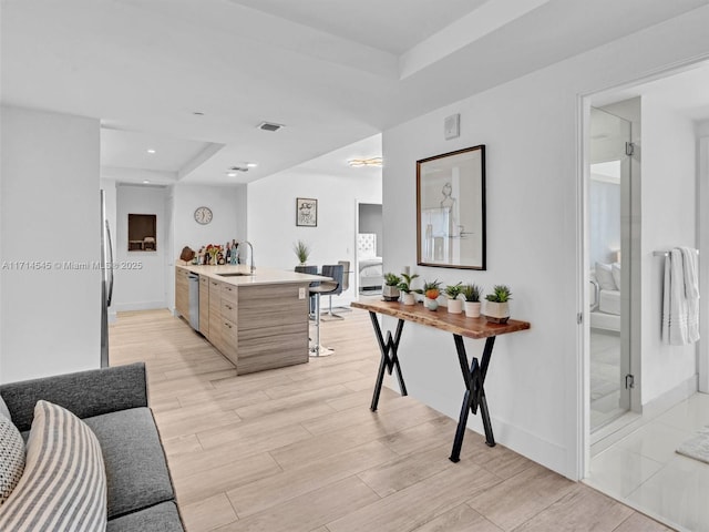 kitchen with a raised ceiling, sink, light brown cabinets, stainless steel appliances, and a center island with sink