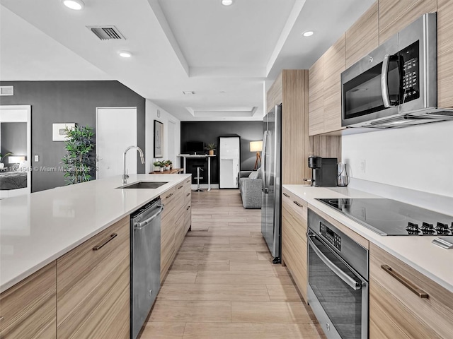 kitchen with sink, light brown cabinets, a raised ceiling, and appliances with stainless steel finishes