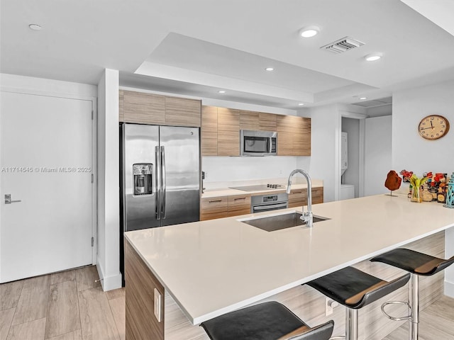 kitchen featuring sink, a breakfast bar area, appliances with stainless steel finishes, kitchen peninsula, and a raised ceiling