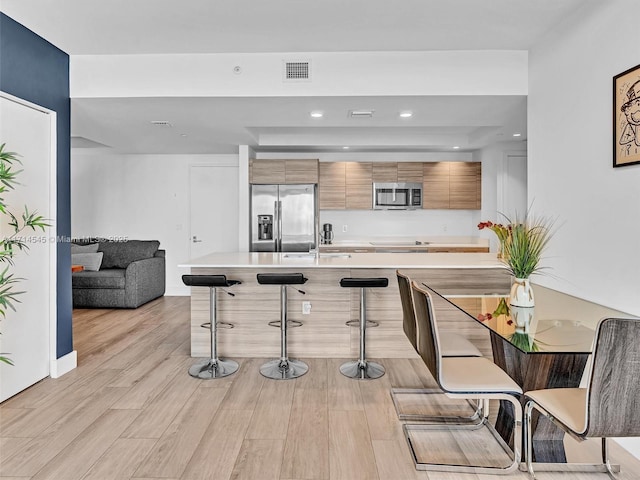 kitchen with sink, stainless steel appliances, light hardwood / wood-style floors, and a kitchen bar