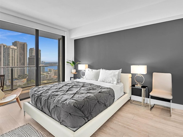 bedroom with floor to ceiling windows, a water view, and light hardwood / wood-style flooring