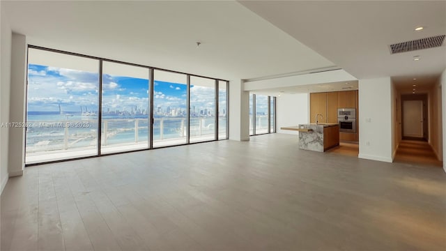 unfurnished living room with sink, a wall of windows, light wood-type flooring, and a water view