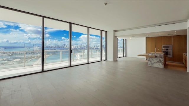 unfurnished living room featuring sink, light wood-type flooring, floor to ceiling windows, and a water view