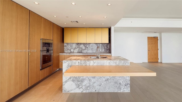 kitchen featuring light wood-type flooring, a spacious island, backsplash, and sink