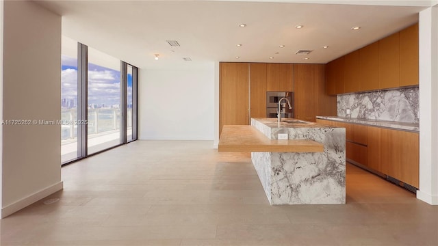 kitchen featuring a center island with sink, floor to ceiling windows, refrigerator, sink, and tasteful backsplash