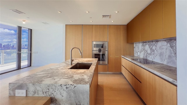 kitchen featuring sink, a wall of windows, stainless steel double oven, backsplash, and black electric stovetop