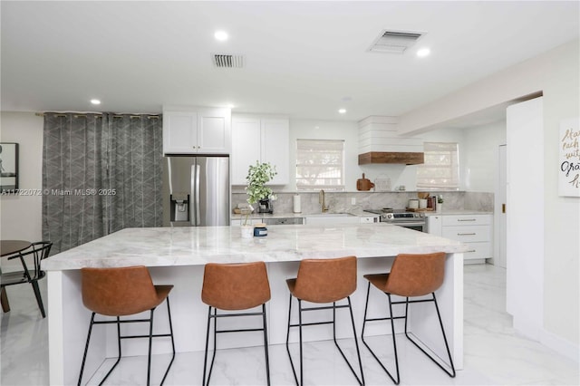 kitchen with stainless steel appliances, white cabinetry, a kitchen bar, light stone countertops, and a kitchen island