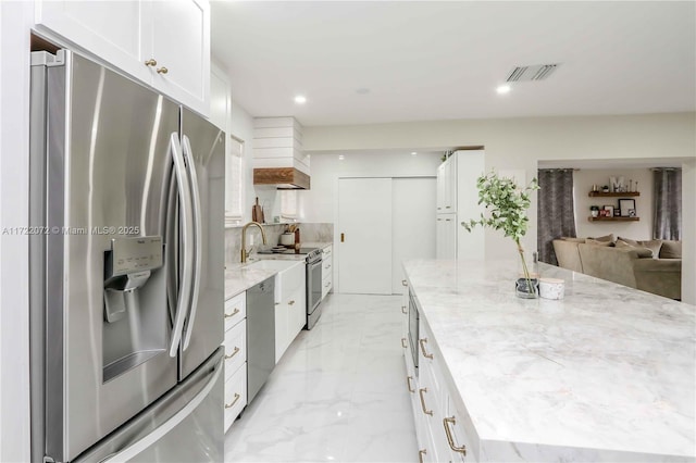 kitchen featuring white cabinets, stainless steel appliances, a center island, and light stone countertops