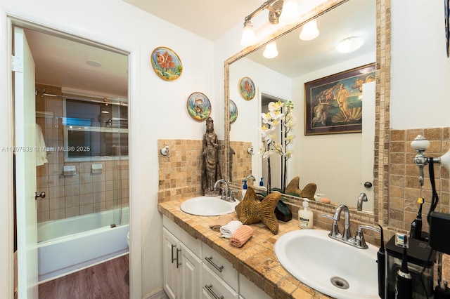 full bathroom featuring hardwood / wood-style floors, toilet, vanity, tiled shower / bath, and backsplash