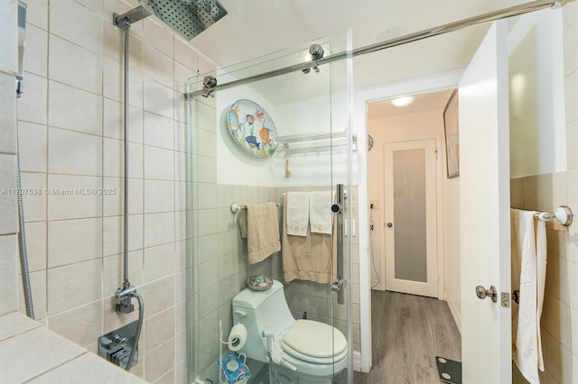 bathroom with wood-type flooring, a shower with door, tile walls, and toilet