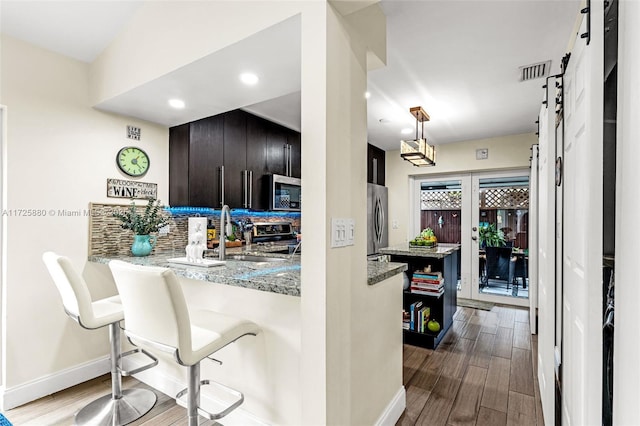 kitchen with stainless steel appliances, kitchen peninsula, a kitchen bar, light stone counters, and sink