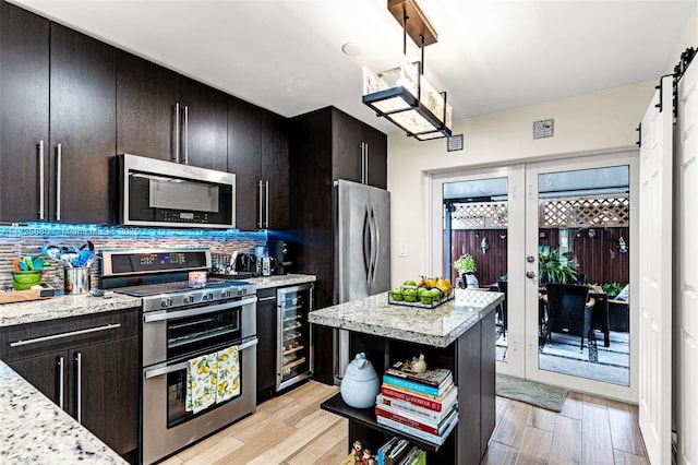 kitchen with stainless steel appliances, light stone counters, beverage cooler, backsplash, and a barn door