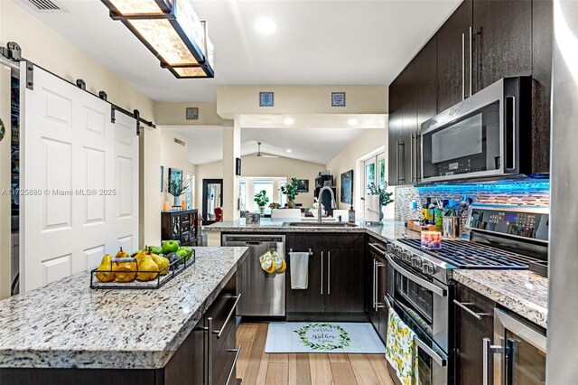 kitchen with stainless steel appliances, sink, lofted ceiling, decorative backsplash, and a barn door