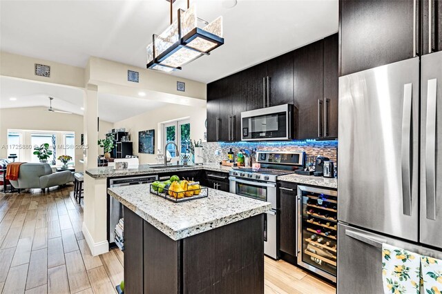 kitchen with beverage cooler, appliances with stainless steel finishes, a center island, kitchen peninsula, and backsplash