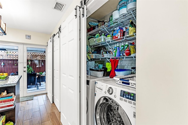 laundry area with a barn door, laundry area, wood finished floors, visible vents, and washer / clothes dryer