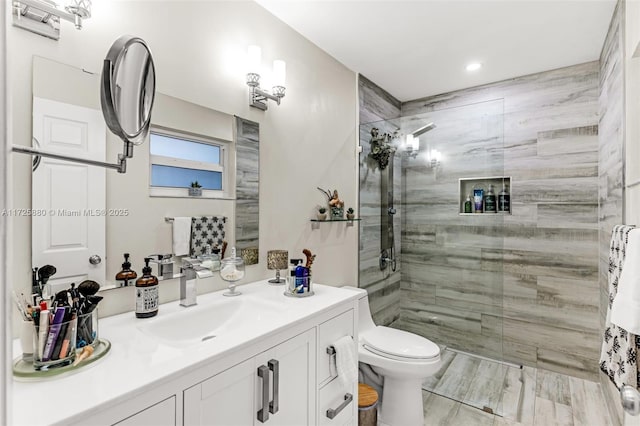 bathroom with toilet, a tile shower, and vanity