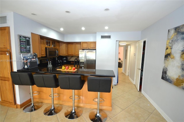 kitchen featuring brown cabinets, a breakfast bar area, stainless steel appliances, visible vents, and a peninsula