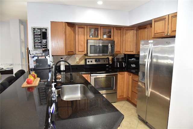 kitchen featuring appliances with stainless steel finishes, decorative backsplash, light tile patterned flooring, dark stone counters, and sink