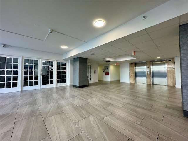 unfurnished room with elevator, french doors, and a drop ceiling