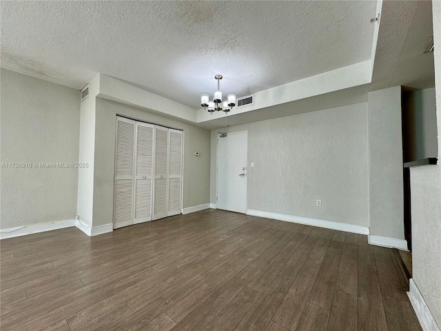 interior space with a textured ceiling, dark hardwood / wood-style flooring, an inviting chandelier, and a tray ceiling