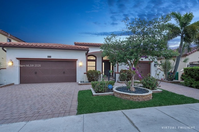 mediterranean / spanish house with a tiled roof, stucco siding, an attached garage, and decorative driveway