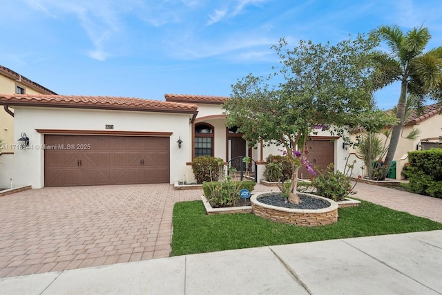 mediterranean / spanish-style house with a tiled roof, stucco siding, an attached garage, and decorative driveway